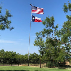 American and Texas flags on a flagpole with green grass and trees in the background